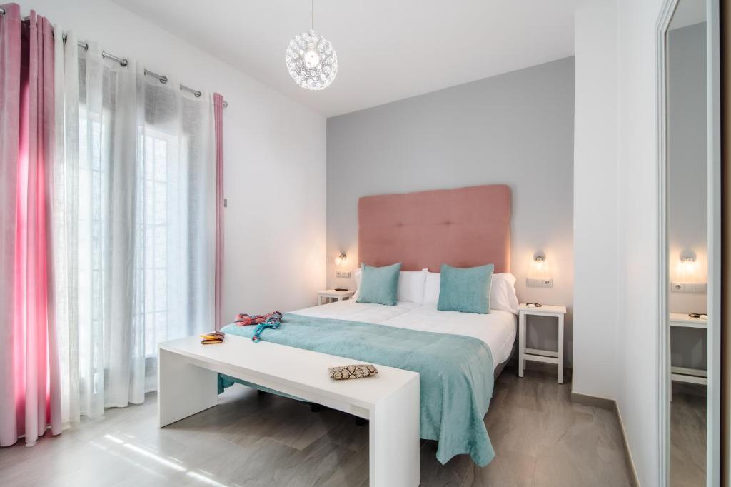 a white bedroom with a large bed and a table at Amphora Alojamiento Ecija in Écija