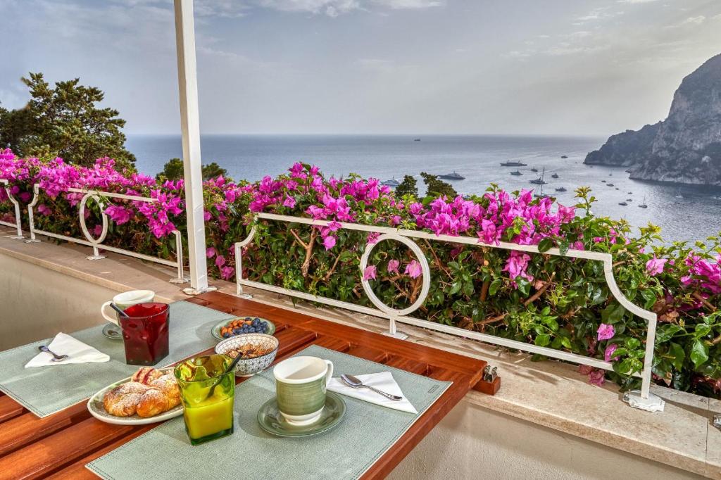 uma mesa com comida numa varanda com flores roxas em Roberhouse Tragara 37 em Capri