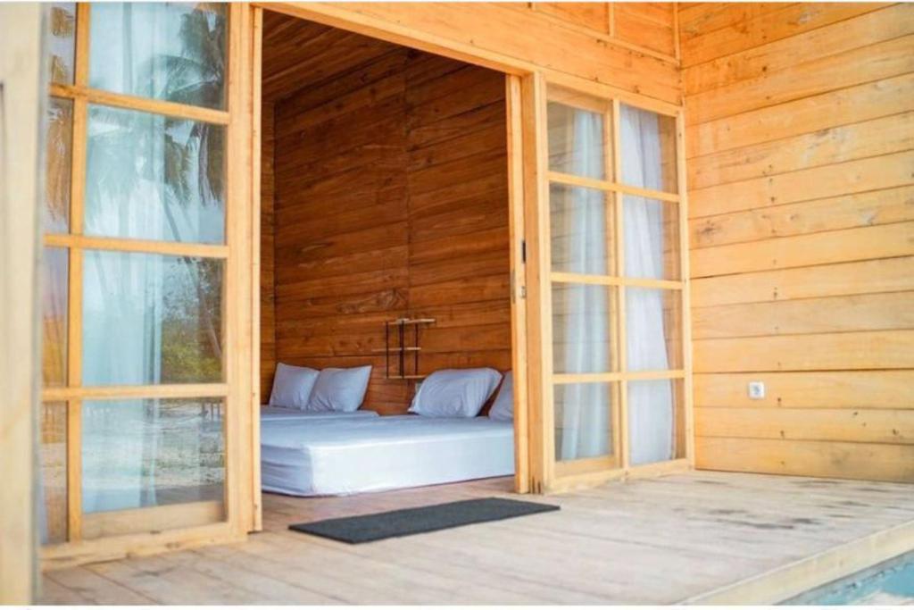 a bed in a wooden room with two windows at Pulau Mahitam Resort & Cottage by Hotelku in Ratai