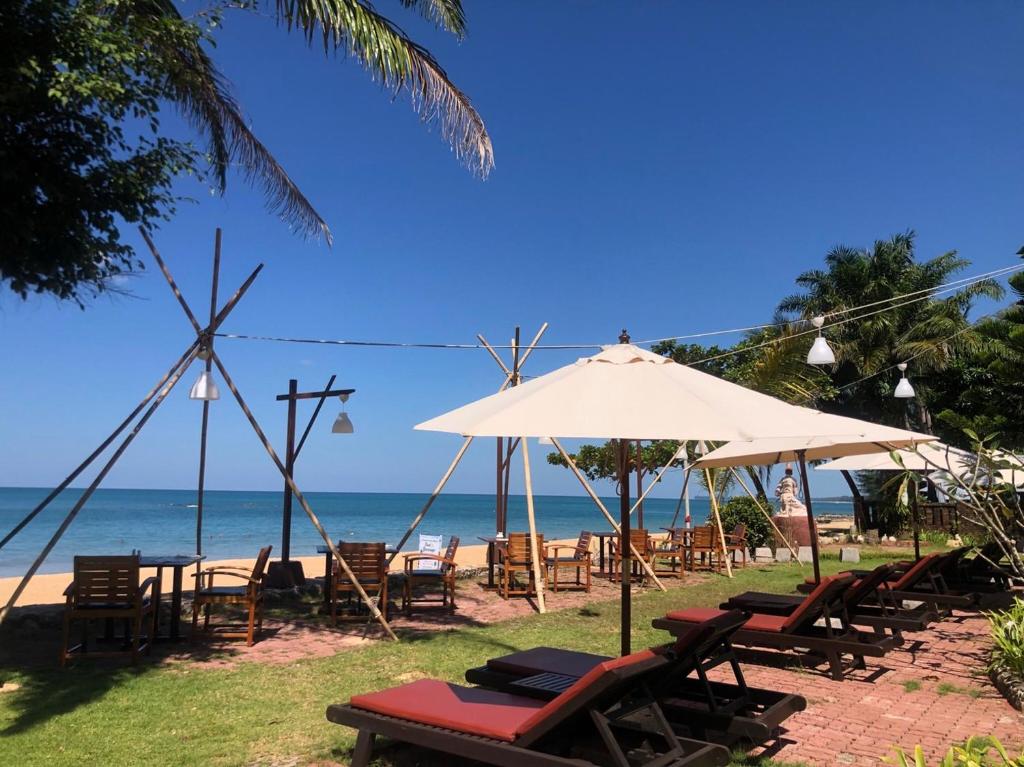 eine Gruppe von Stühlen und Sonnenschirmen am Strand in der Unterkunft Khaolak Palm Beach Resort in Khao Lak