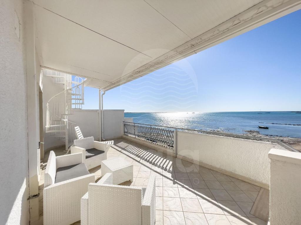 Un balcón con sillas blancas y vistas al océano. en Casa Namaka - Piano Primo Fronte mare, en Porto Cesareo