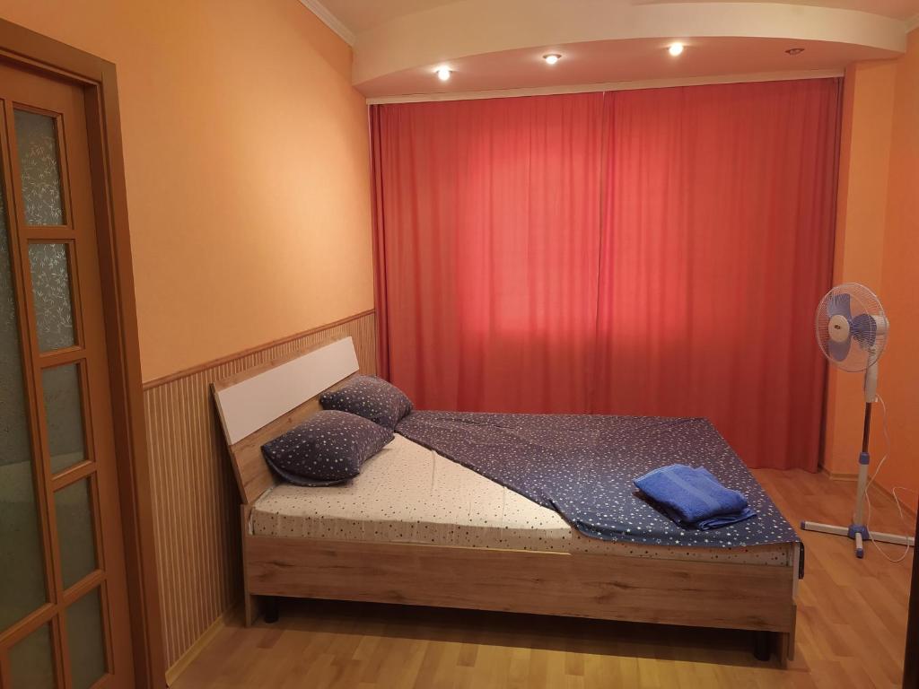 Уютная однокомнатная квартира в г. Бровары في بوفاري: غرفة نوم بسرير وستارة حمراء