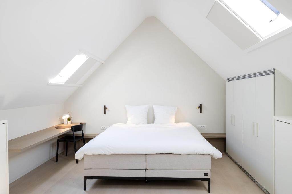 a white bedroom with a bed and a desk at GLUK in Zonnebeke