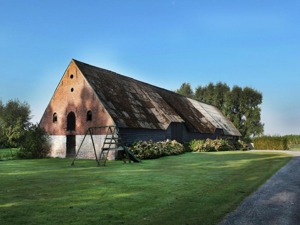 een oude rode bakstenen schuur met een schommel bij Comfortable flat overlooking orchards in Eede