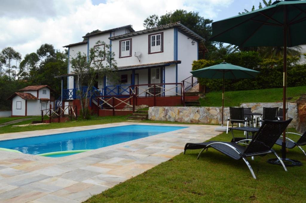 ein Pool mit Stühlen und einem Sonnenschirm und ein Haus in der Unterkunft Pousada Villa Verde in Lavras Novas