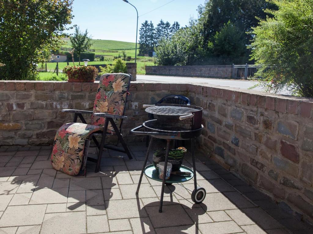 a grill and chairs on a patio next to a brick wall at Quiet apartment along a stream in Halenfeld in Sellerich