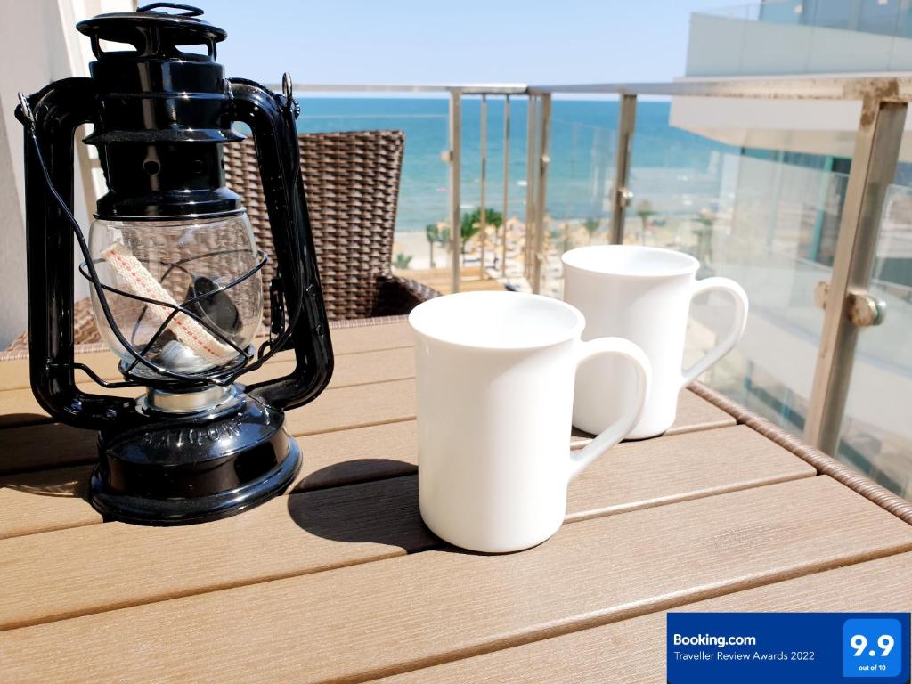 - deux tasses à café blanches et un mixeur sur un balcon dans l'établissement Seaview studio private parking included - Beach Residence, à Mamaia Nord – Năvodari