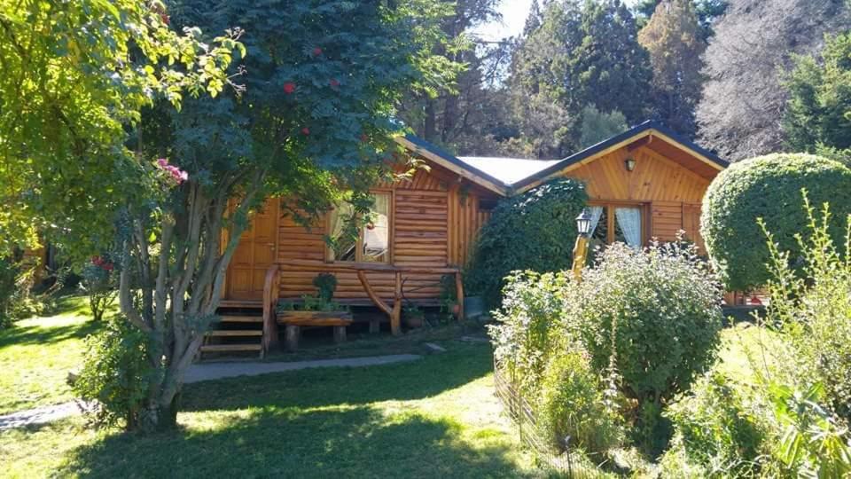 une cabane en rondins avec une terrasse couverte dans un jardin dans l'établissement CABAÑAS MANOLO, à San Carlos de Bariloche