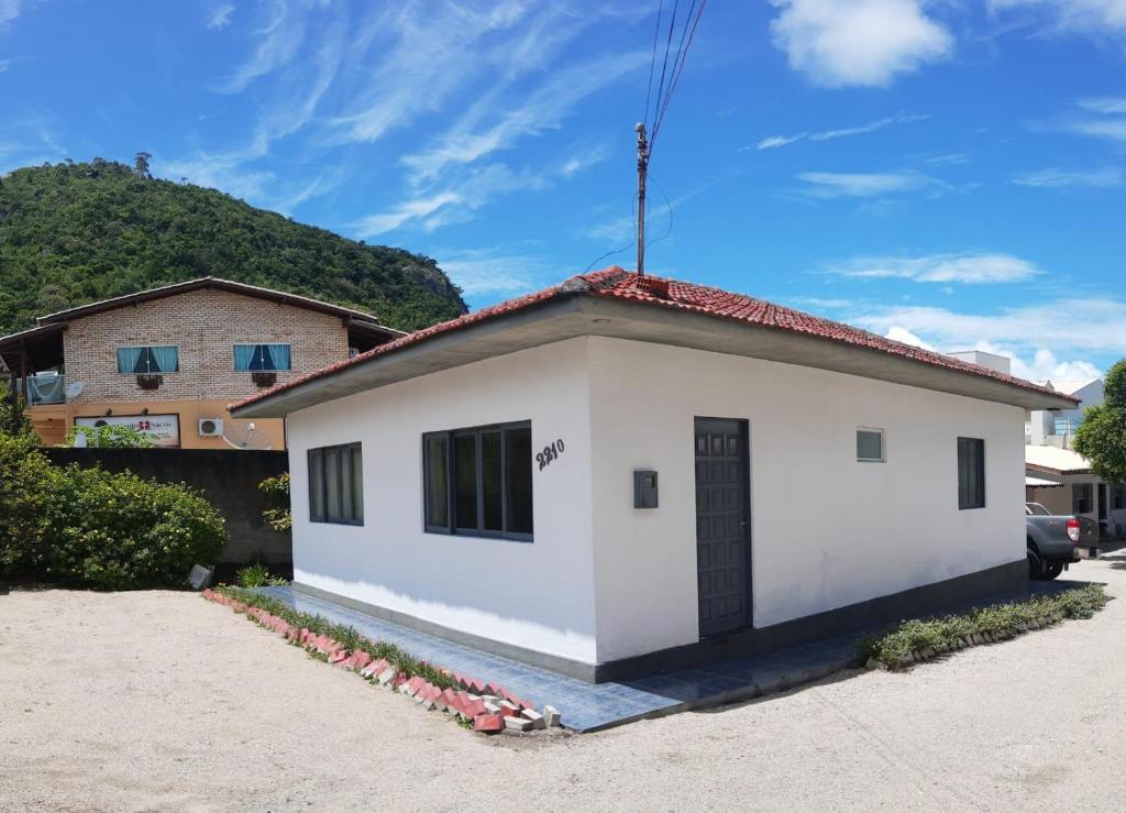 una pequeña casa blanca con una colina en el fondo en Casa com Pôr do Sol em Canto Grande - Casa Beira Mar Bombinhas, en Bombinhas