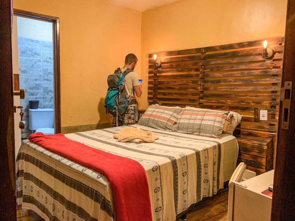 un hombre parado en un dormitorio con una cama en Pousada Aconchego - Suítes Rústicas e Privativas, en Lençóis