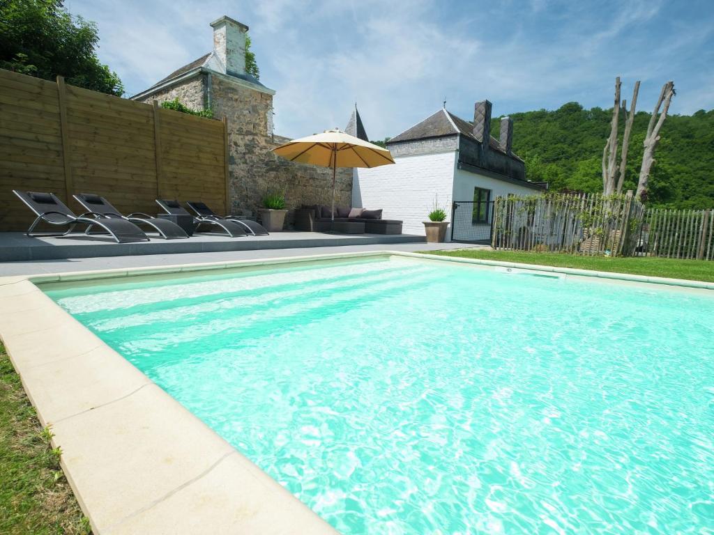 a swimming pool with chairs and an umbrella at Stylish Mansion in Ardennes with shared Pool in Hastière-par-delà