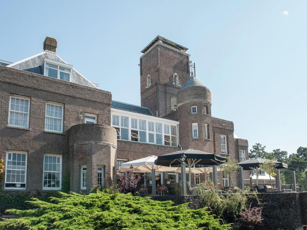 un gran edificio de ladrillo con una sombrilla delante de él en Unique studio on large estate with sea view, en Bergen aan Zee