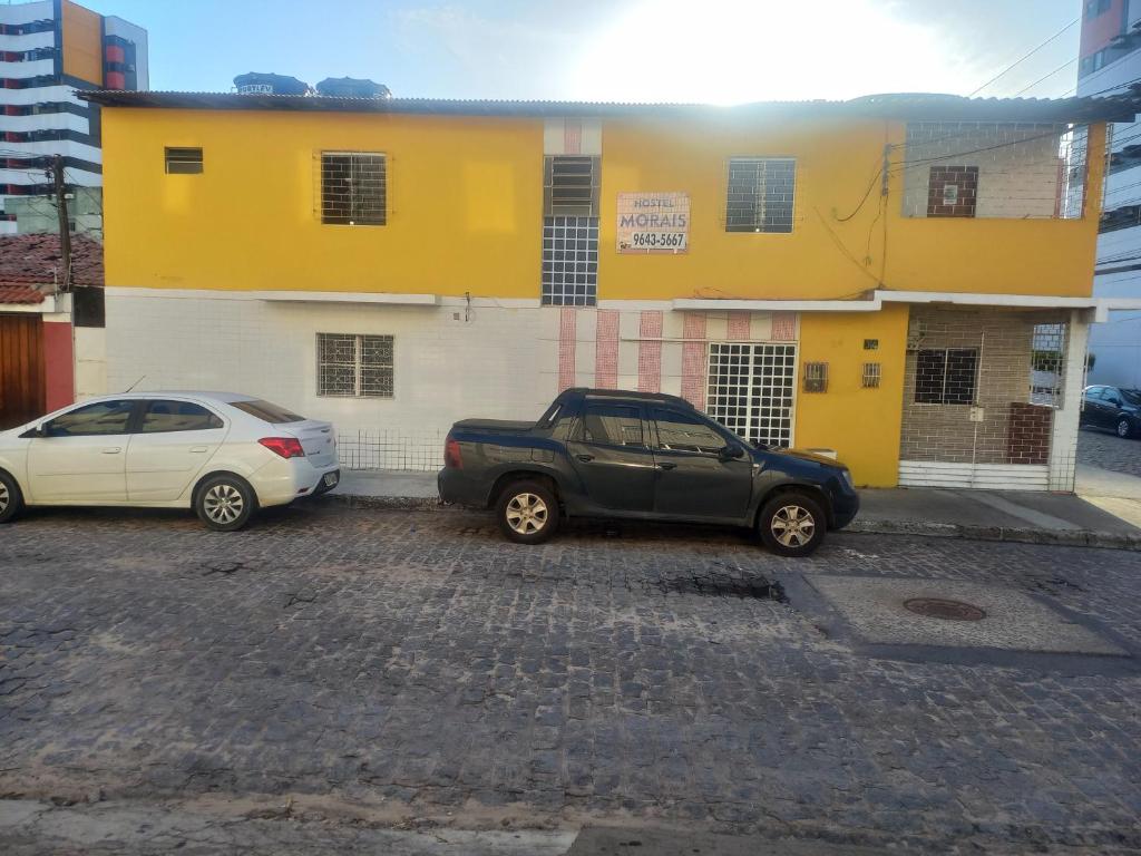 two cars parked in front of a yellow and white building at Hostel Morais in Maceió