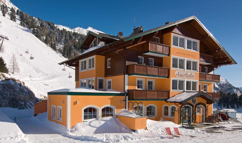un grand bâtiment dans la neige devant une montagne dans l'établissement Hotel & Appartement Auerhahn, à Obertauern