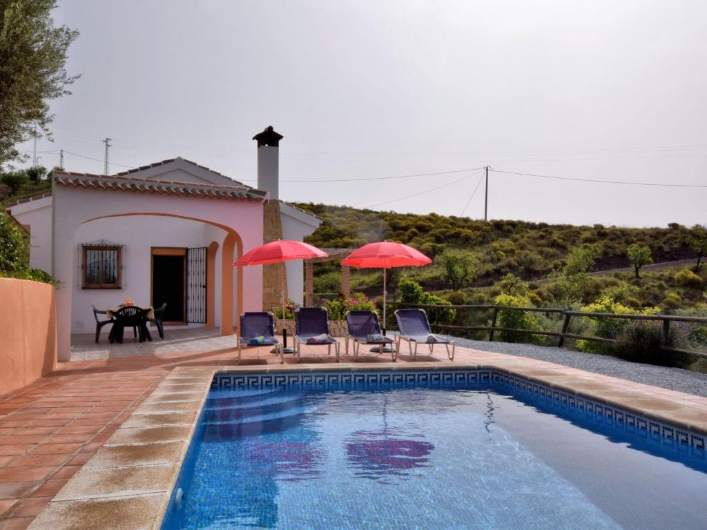 Árchez的住宿－Belvilla by OYO Casa Guzm n，一个带两把遮阳伞和椅子的游泳池以及一座房子