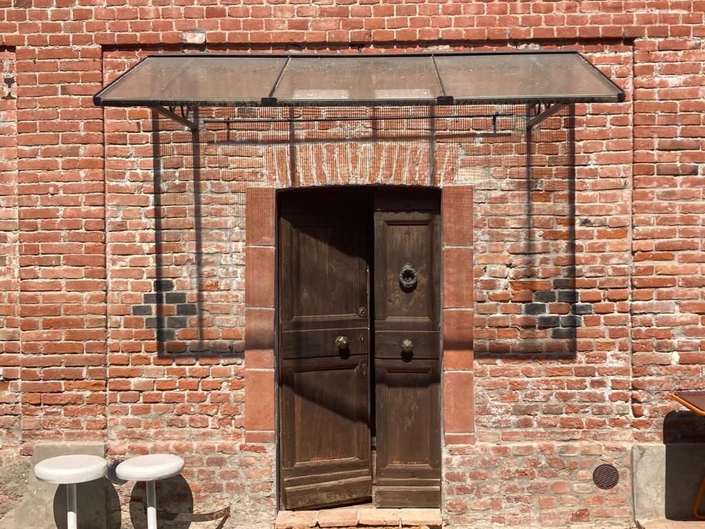 un edificio de ladrillo con una puerta de madera y dos taburetes en Casa Dormiveglia, en Montaldo Bormida