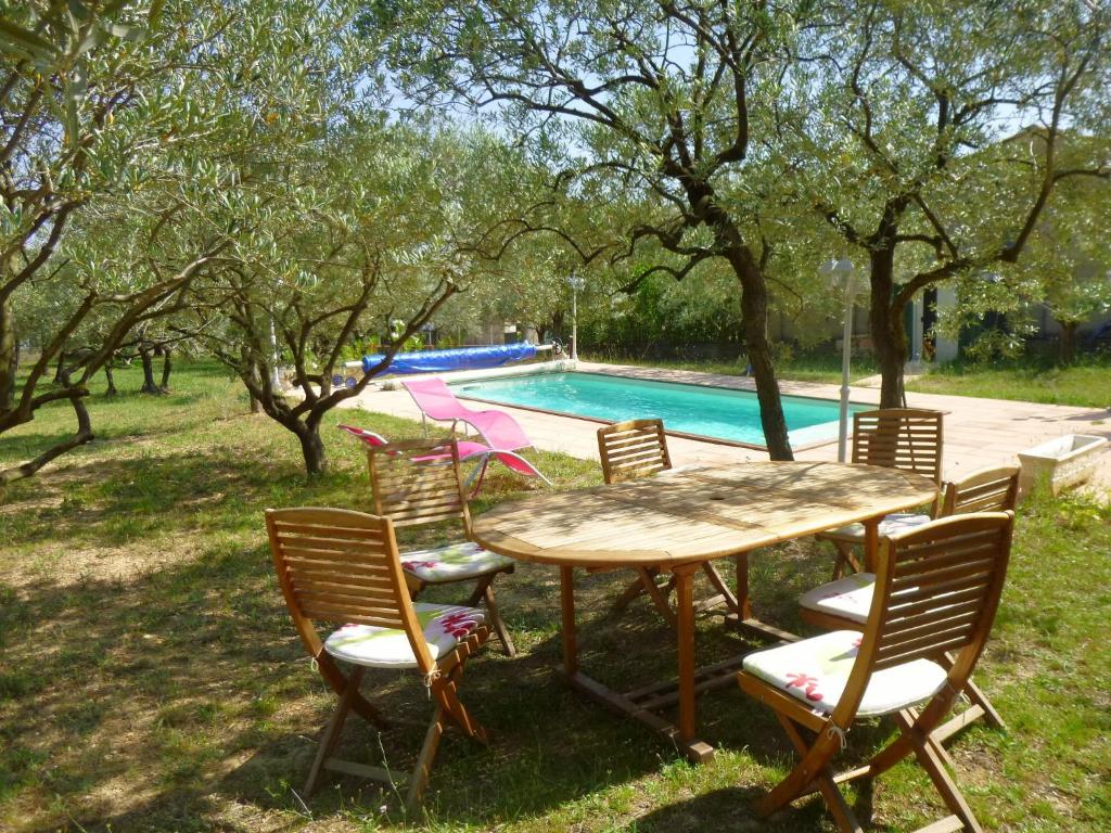una mesa de madera y sillas junto a una piscina en L'Oliveraie en La Motte-dʼAigues