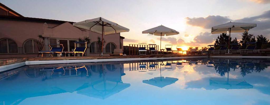 a swimming pool with chairs and umbrellas at sunset at Toscana Wellness Resort in Arcidosso