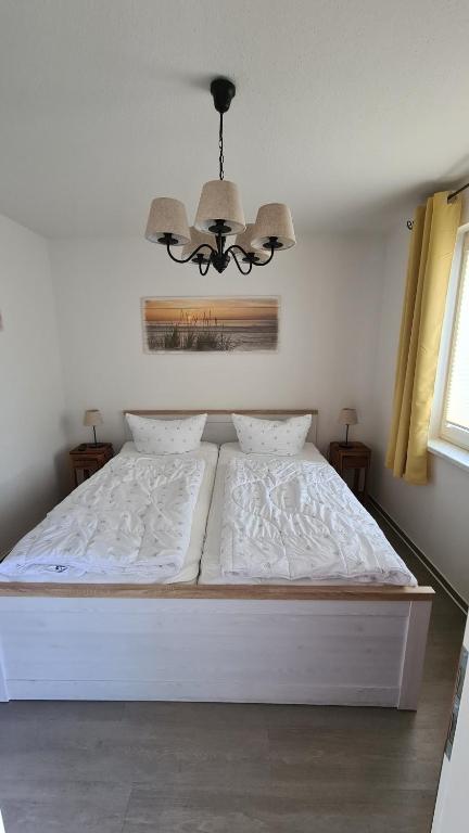 un letto bianco in una camera da letto con lampadario a braccio di Lieblingsplatz im Küstenwald Graal-Müritz a Gelbensande