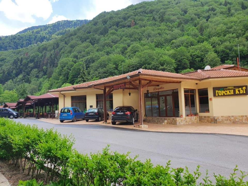 a building with cars parked in front of a mountain at Family Hotel Gorski Kut in Rilski Manastir