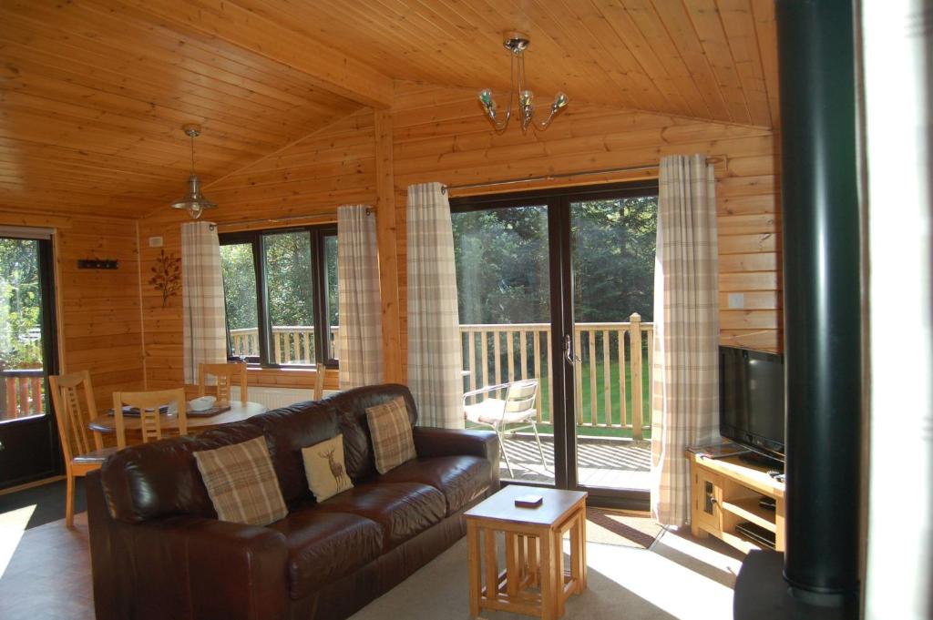a living room with a leather couch and a television at Luxury woodland Alder Lodge in Killin