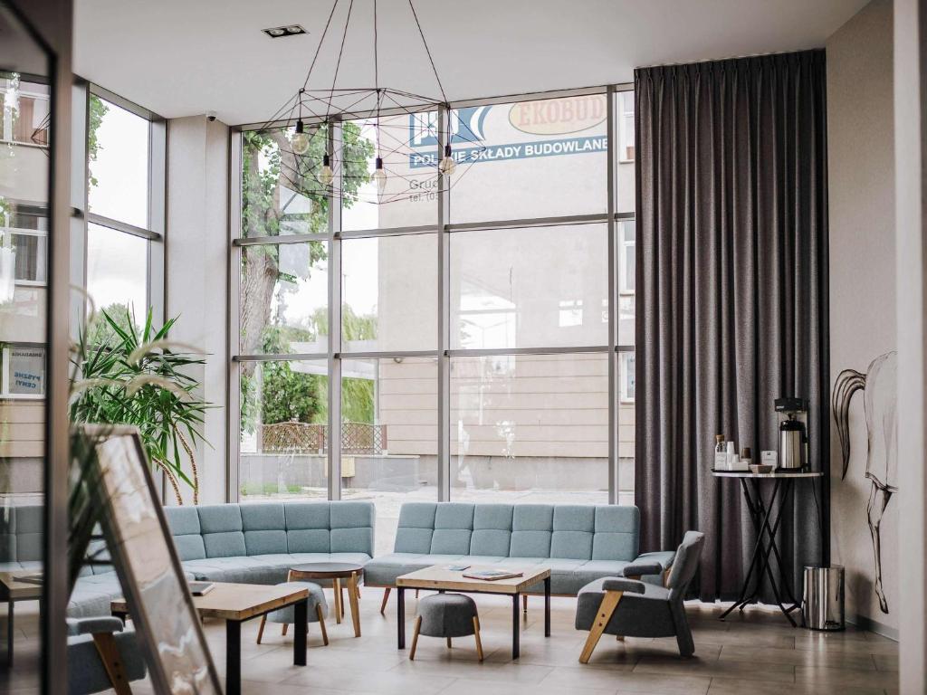 a living room with a blue couch and a large window at ibis styles Grudziadz in Grudziądz