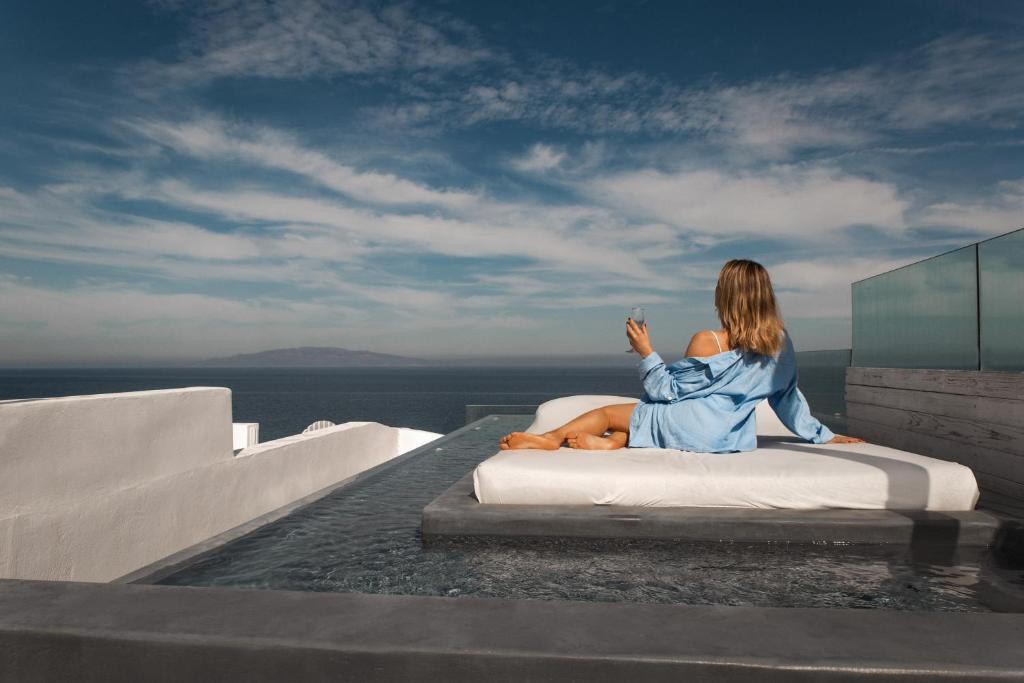 a woman sitting on a bench near a body of water at Almyra Oia Suites in Oia
