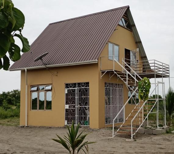 a yellow house with a metal roof and a staircase at Bagamoyo Home Stay in Bagamoyo