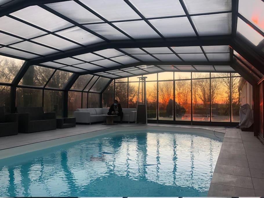 a pool in a greenhouse with a person sitting on a couch at Maison Normande - PISCINE chauffée couverte in Morainville-près-Lieurey