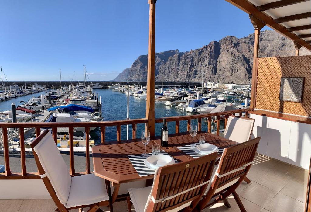een houten tafel en stoelen op een balkon met een jachthaven bij Top View Acantilados de Los Gigantes in Acantilado de los Gigantes