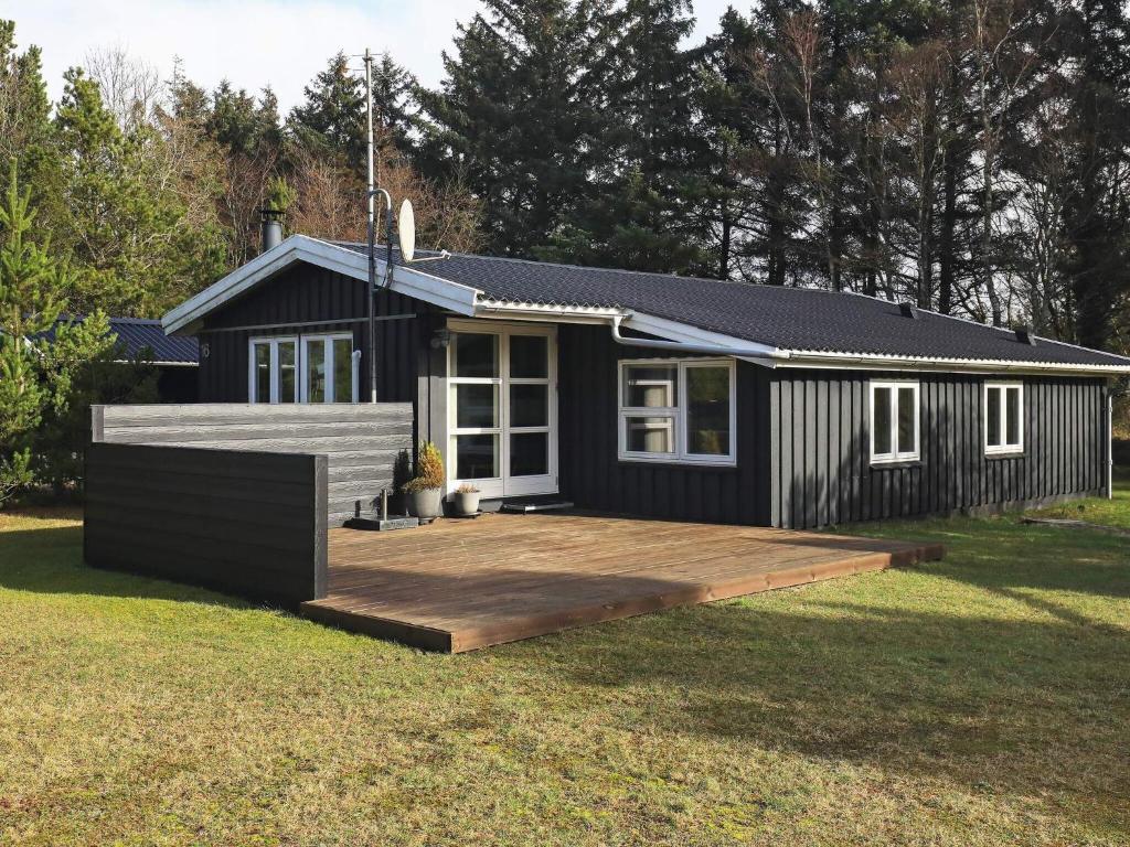 una pequeña casa negra con una gran terraza en 6 person holiday home in Bl vand, en Blåvand