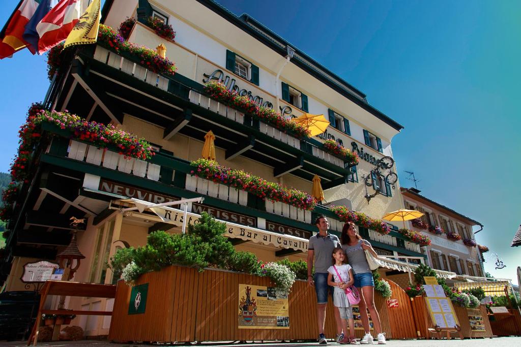Un uomo, una donna e un bambino in piedi davanti a un palazzo di Hotel Cavallino Bianco - Weisses Roessl a San Candido
