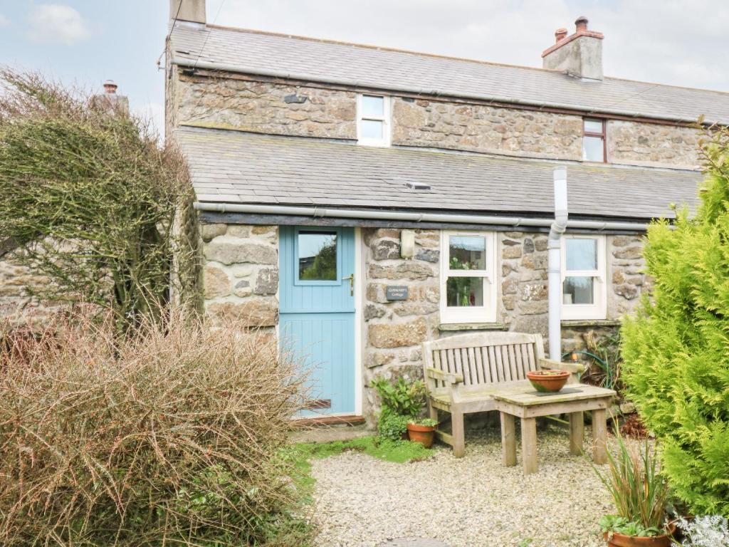 um chalé de pedra com uma porta azul e um banco em Gurnard's Cottage em Treen