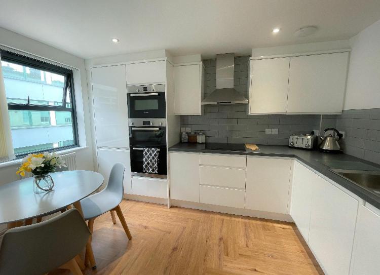 une cuisine avec des placards blancs, une table et une salle à manger dans l'établissement Prosper House Apartments, à Norwich