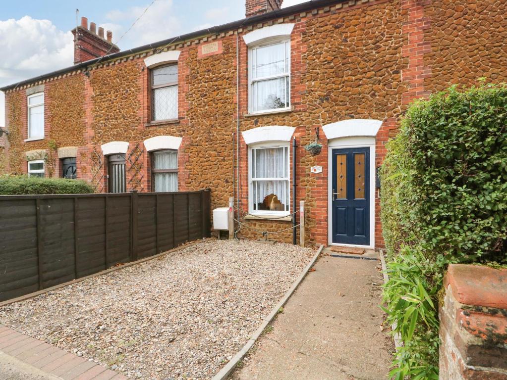 une maison en briques avec une porte bleue et un chien assis à la fenêtre dans l'établissement Duck Cottage, à Snettisham