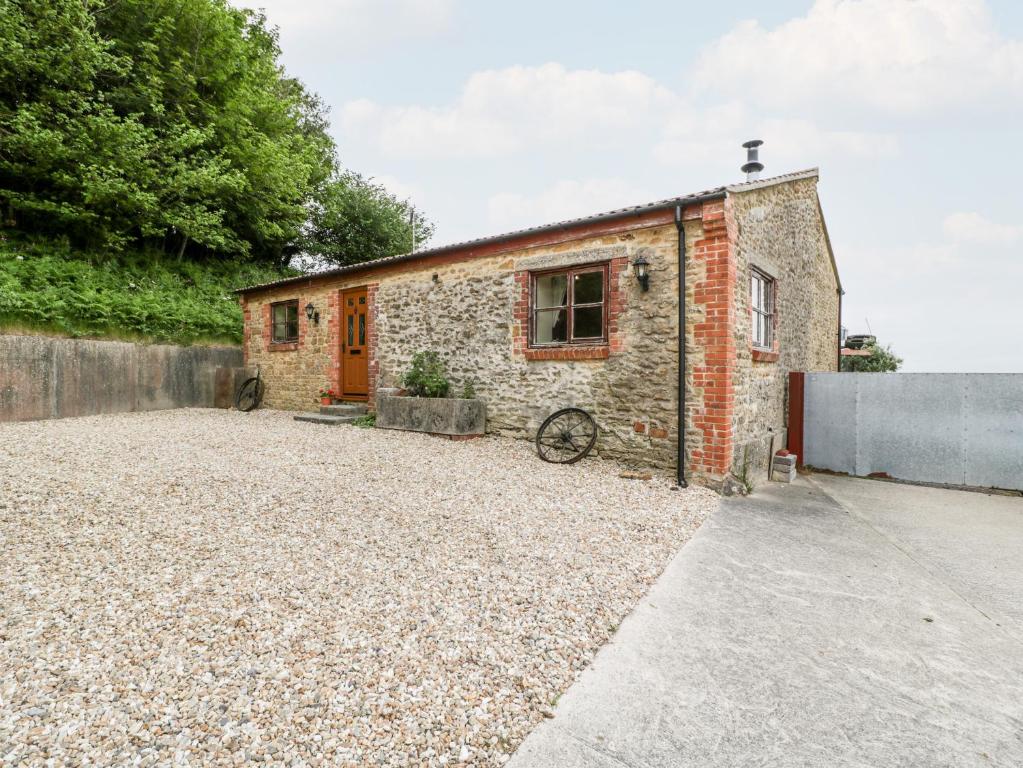 a stone house with a red door on a gravel driveway at The Barn in Beaminster