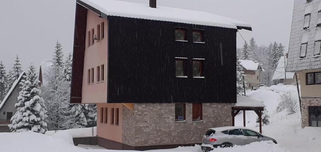 a building with a black roof in the snow at Apartments Gaga in Jahorina