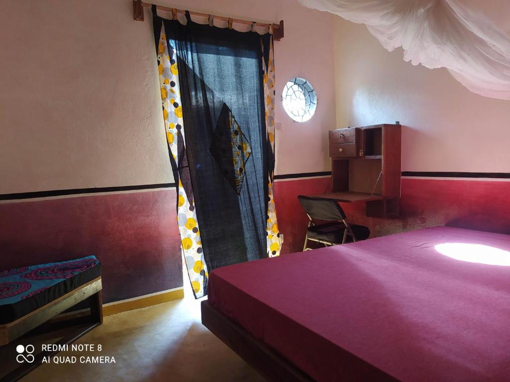 a bedroom with a bed and a table and a window at Chez Yaya - Chambre Sousete in Oussouye