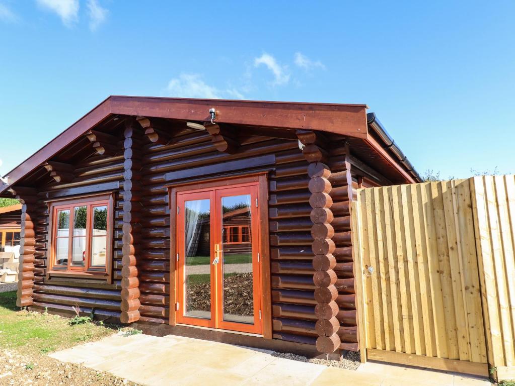 a log cabin with red doors and a fence at Pine Lodge in Oakham