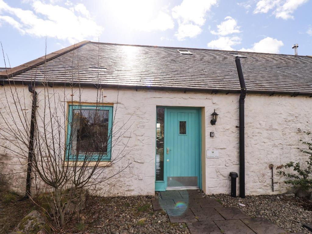 un pequeño edificio blanco con una puerta azul en Sweetheart Cottage, en Dalbeattie