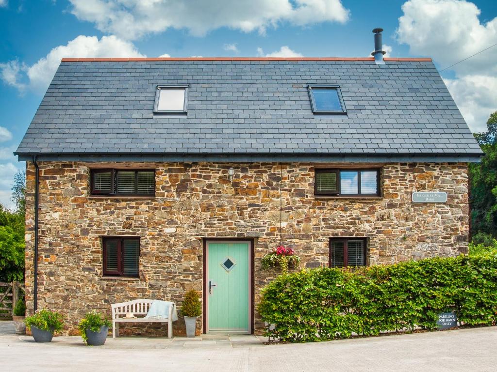 una casa in pietra con una porta verde e una panchina di Brightley Mill Barn a Okehampton