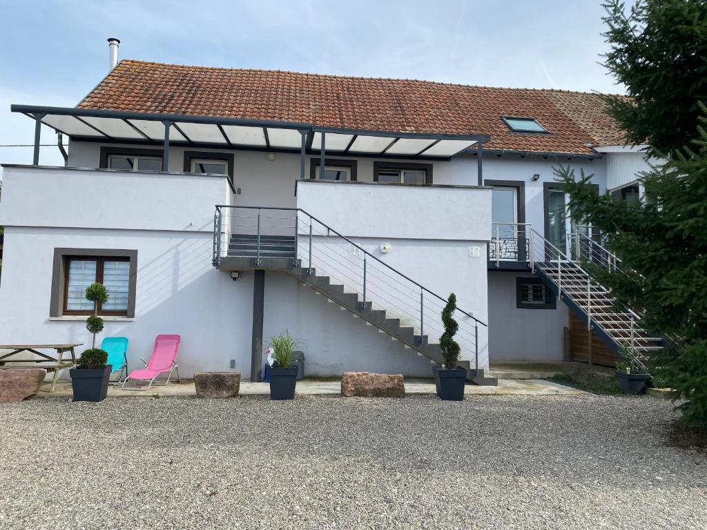 a white house with a staircase and a pink chair at Gites Bretzel et Cigogne in Munwiller