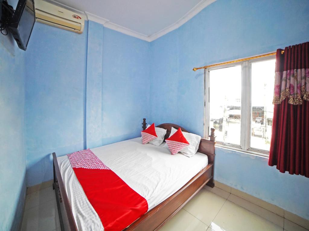 a bedroom with a bed with blue walls and a window at OYO 90922 Gurusinga Guesthouse in Medan