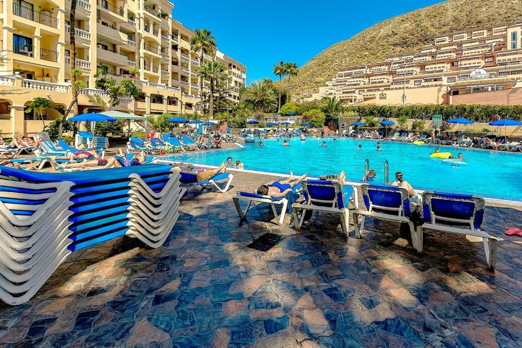 a pool with people sitting in chairs in a resort at One Bedroom Apartment - Los Cristianos in El Guincho