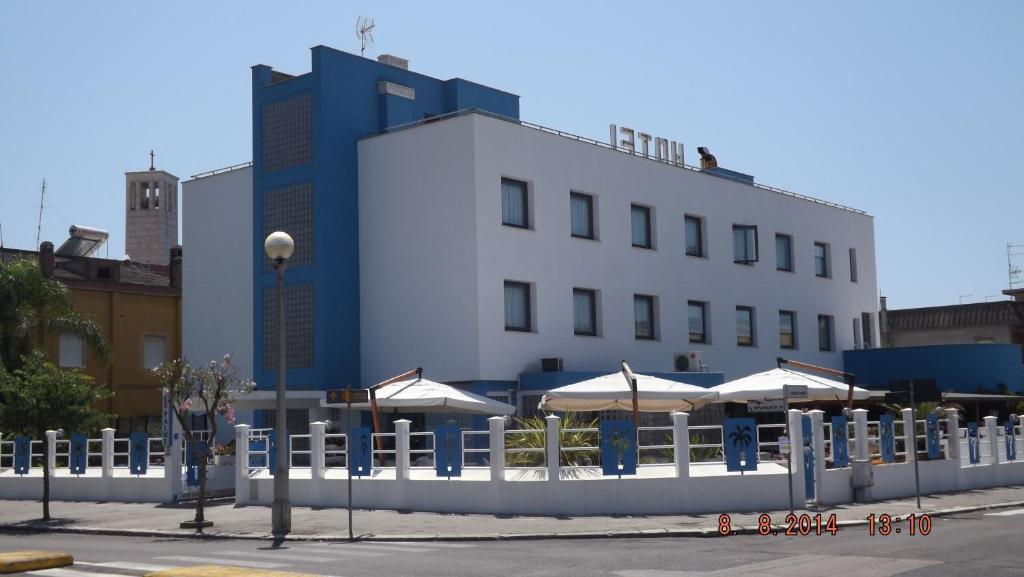 a white fence in front of a building with umbrellas at Hotel Le Palme in Sabaudia