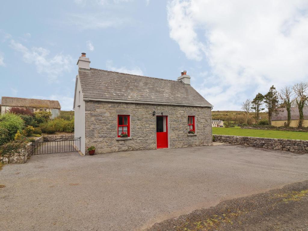 um pequeno edifício de pedra com uma porta vermelha em Limestone Cottage em Ennis