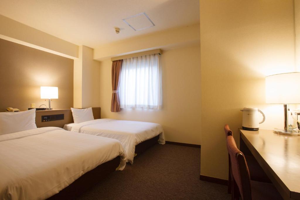 a hotel room with two beds and a desk and a window at Sankei City Hotel Chiba in Chiba