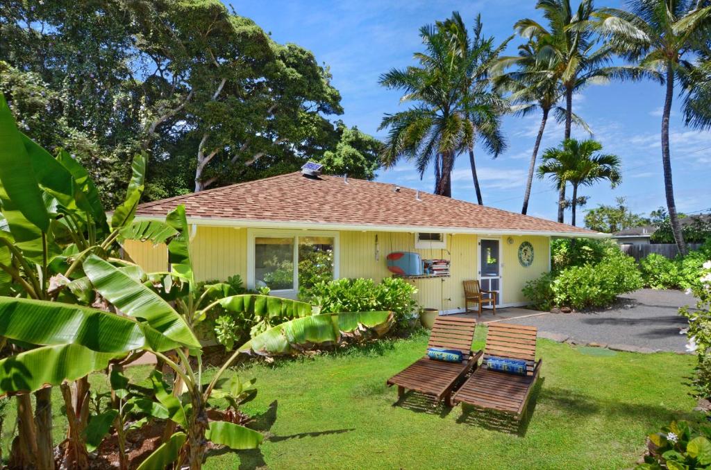 a small yellow house with two benches in the yard at Melemele Kapaa Cottage 1 Block to Beach! in Kapaa