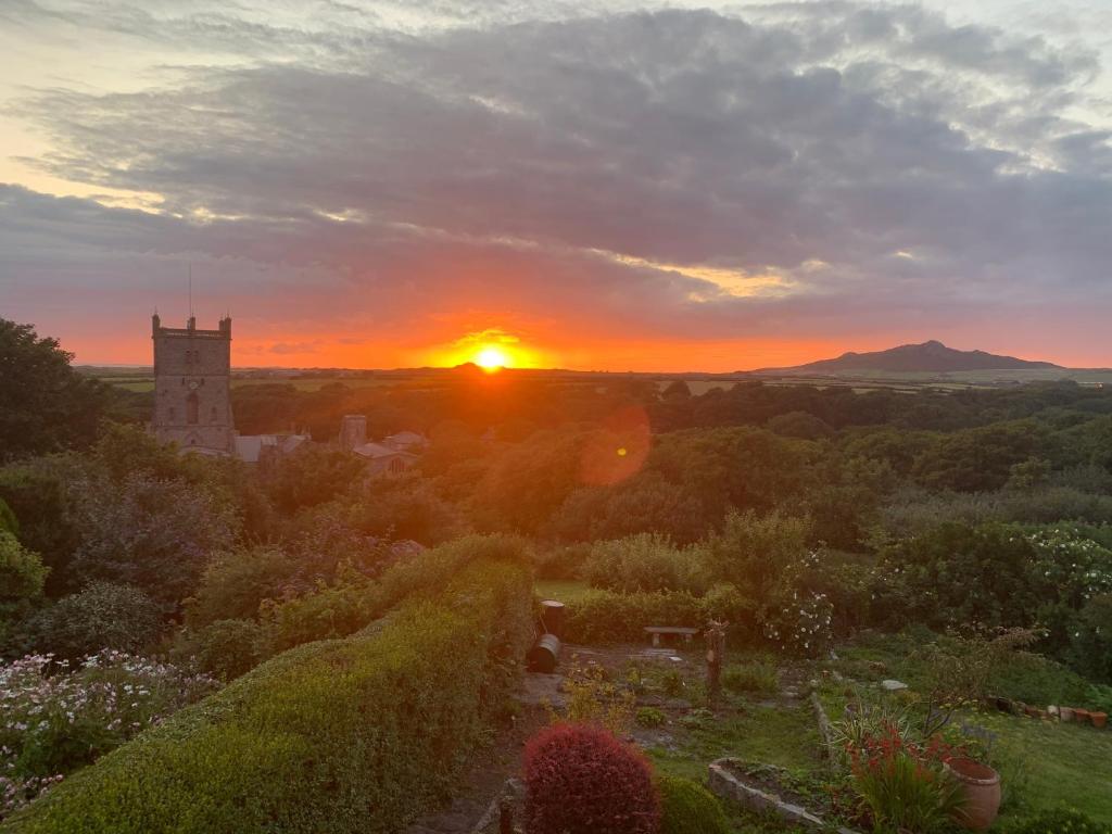 una puesta de sol sobre un jardín con una torre de reloj en St Davids Gin & Kitchen - The Cathedral Villas en St. Davids