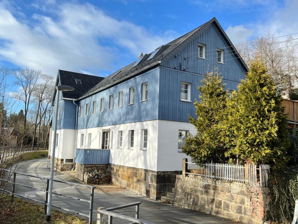 ein blau-weißes Gebäude mit schwarzem Dach in der Unterkunft Ferienwohnung Idyll am Weigsdorfer Teich in Cunewalde